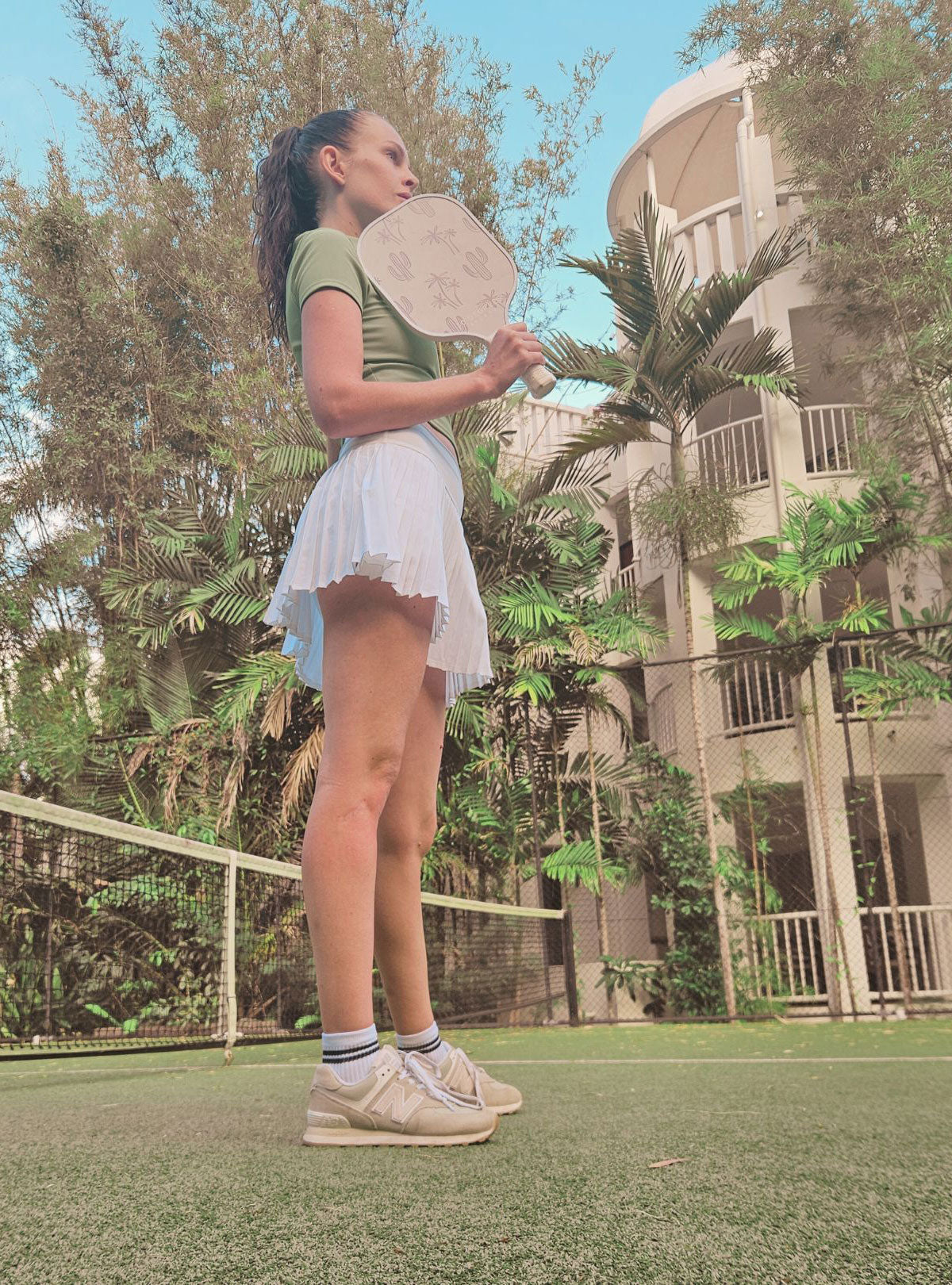 female pickleball player holding palm pattern pickleball paddle on a court